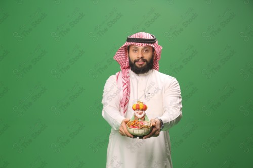 بورتريه رجل سعودي يرتدي الزي السعودي التقليدي يحمل سلة حلويات ويقدمها لأحدهم