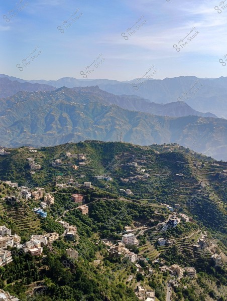 Aerial view of a lush green mountainous area with small villages and scattered houses, surrounded by agricultural terraces. In the background, a series of distant mountains is visible under a clear blue sky.