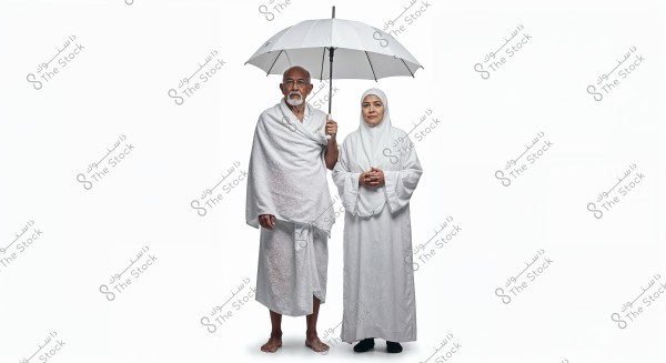 A man and woman wearing white ihram clothing specific for performing Hajj or Umrah. The man holds a large white umbrella. Both stand side by side against a white background, with the man wearing two white garments and the woman in a white abaya and hijab.