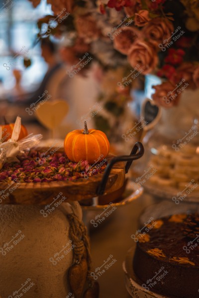 Autumn decoration featuring a small pumpkin on a tray decorated with dried flowers, with a background of pink roses.