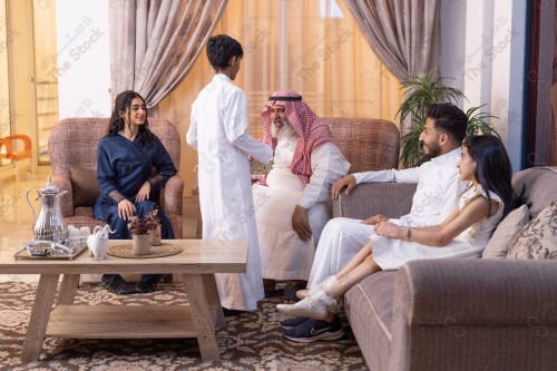 A child in traditional Saudi dress carries a basket of sweets and presents it to his family, family meeting in the living room on Eid morning