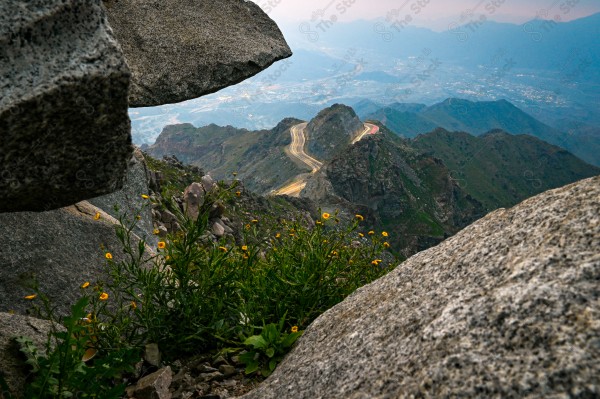 A snapshot of a series of towering rocky mountains and paved roads extending in the Al Hada Mountains in Taif, showing a cloudy sky during the day, mountain heights, Taif Mountains, mountain range