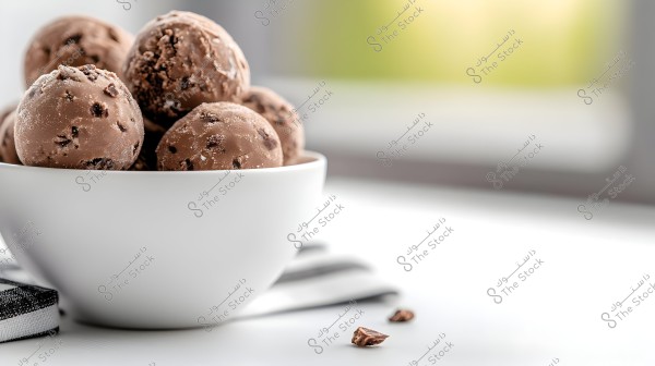 An image showing a white bowl containing several scoops of chocolate chip ice cream. The bowl is placed on a white surface with a blurred background suggesting natural lighting.