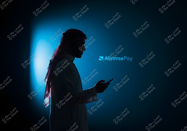 Image of a man wearing a traditional thobe and ghutra, standing in profile while using a smartphone. The background is dark with a prominent blue light behind him, and the \"Alinma Pay\" logo is visible on the right side of the image.