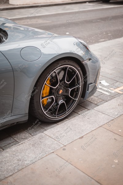 Image of a gray sports car with a black wheel and yellow brake calipers on the street.