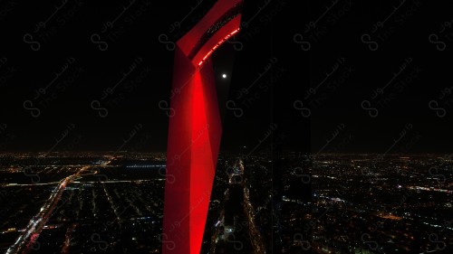 A shot showing the buildings and landmarks of the city of Riyadh, in front of it a group of residential houses, and the sky is clear at night