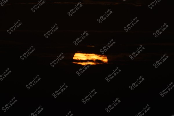 The image shows a sunset with the orange disk of the sun partially obscured by dark clouds, creating a dramatic scene in the evening sky. The clouds on the horizon are dark, adding a mysterious atmosphere.