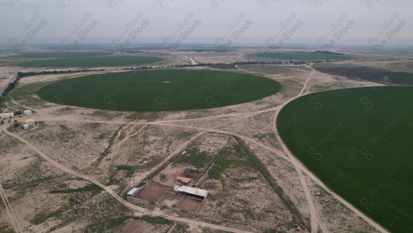 منظر جوي لحقول زراعية دائرية وسط أرض صحراوية، مع وجود مجموعة من المباني والطرق الجانبية.