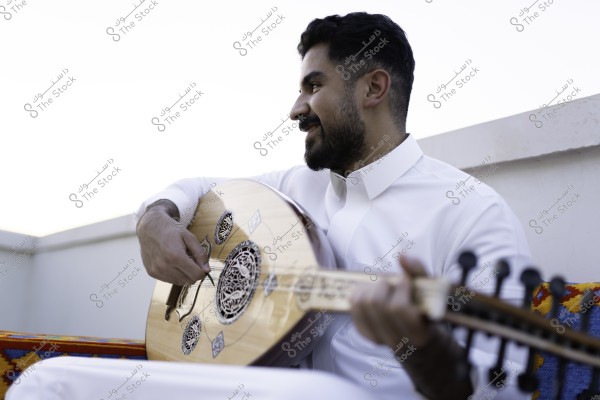رجل يعزف على العود وهو يرتدي ثوبًا أبيض, جالس على أريكة مزخرفة بألوان مبهجة.