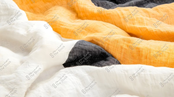 An image showing pieces of fabric in different colors including white, black, and orange. The fabric appears soft and lightweight with a subtle texture.