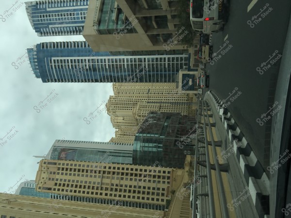 High-rise buildings on a cloudy day, showing a cluster of skyscrapers in different colors, with several vehicles driving on the road next to metal safety barriers.