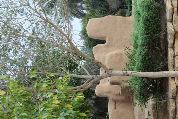 An image of a brown adobe wall surrounded by green trees and various plant leaves. In the background, construction stones and diverse plants create an impression of a natural environment or a garden.\r\n\r\n###
