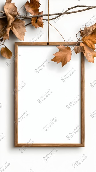 A wooden empty frame hanging on a tree branch adorned with fallen brown leaves. The background is a clean white, highlighting the dry leaves and slender branch.