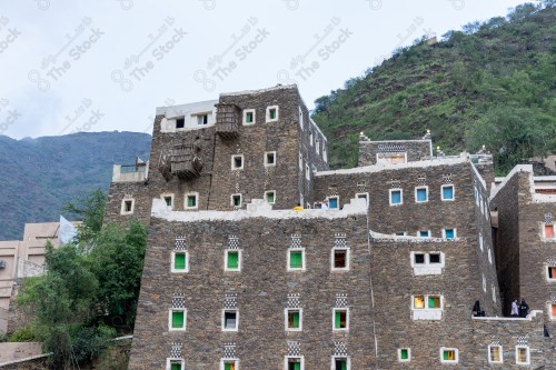 An ancient building built of stones in the middle of a group of windows surrounded by white paint while the sky looks cloudy during sunset, Rijal Almaa Heritage Village in the Asir region