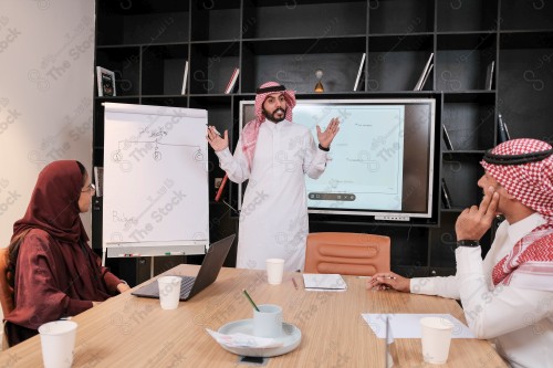 A Saudi man in traditional Saudi dress conducts a business meeting in the boardroom during the day