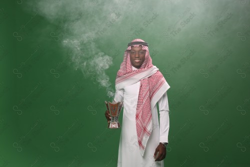 رجل سعودي يرتدي الزي التقليدي على خلفية خضراء ، التطيب بالبخور والعود ، استخدام خشب العود في المناسبات والأعياد.