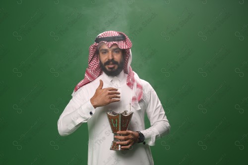 بورتريه رجل سعودي يرتدي الزي السعودي التقليدي يحمل المبخرة ويتطيب بالبخور