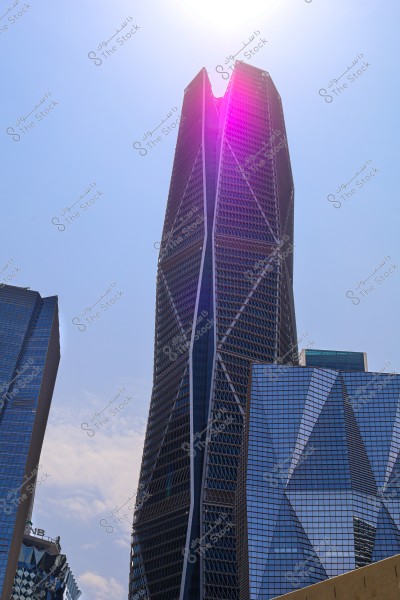 An image of a modern skyscraper with a unique architectural design, centered in the frame with distinctive triangular shapes and geometric lines. The building towers high under a clear blue sky with sunlight reflecting off its glass and metal facade. Other buildings are visible in the background, highlighting the urban skyline.