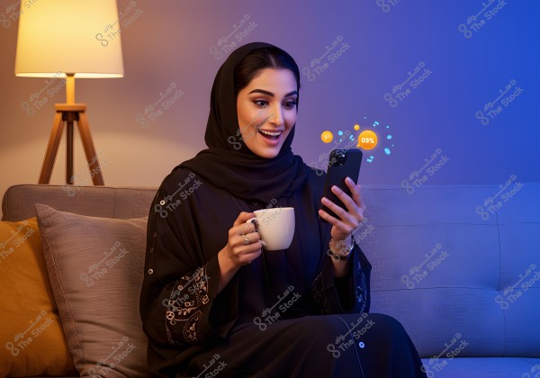 An image of a woman sitting on a sofa in a room with warm lighting from a lamp beside her. She is wearing a black abaya with intricate designs and a black headscarf. She looks delighted as she holds a mobile phone in one hand and a coffee cup in the other. Digital symbols appear around the phone, suggesting a tech interaction.