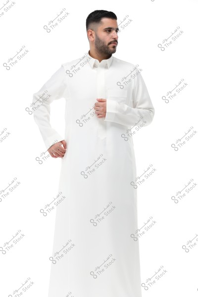 Photo of a man wearing a traditional white thobe, looking to the right side. The thobe is part of traditional attire in Saudi Arabia. The background is white and plain.