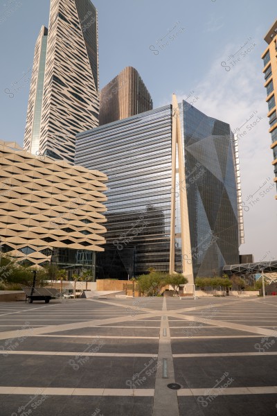 The image shows a collection of modern, high-rise buildings in an urban area, featuring diverse architectural designs with glass facades and unique geometric structures. The ground is paved and clean, with some trees and solar panels in the foreground.