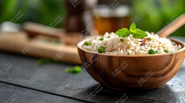 A close-up image of a bowl of white rice in a wooden dish, garnished with green peas and fresh mint leaves. The bowl is placed on a dark tabletop, with some utensils visible in the background.