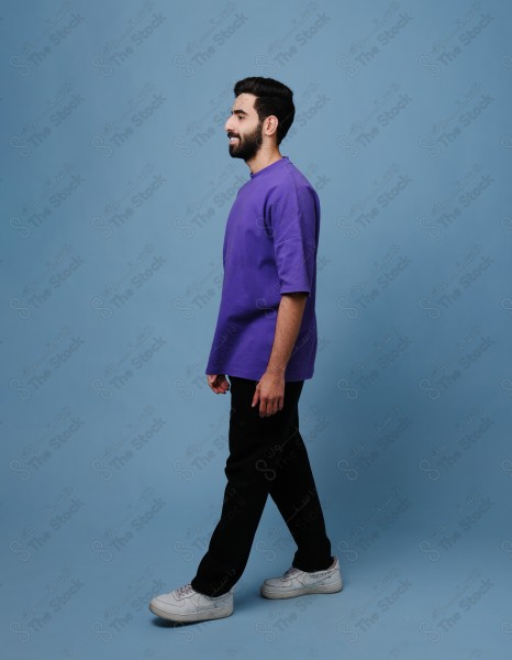 Portrait of a smiling Saudi youth, standing on a blue background.