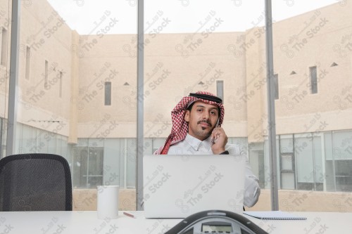 A Saudi man wearing the Saudi thobe sits in the meeting room and uses the mobile device