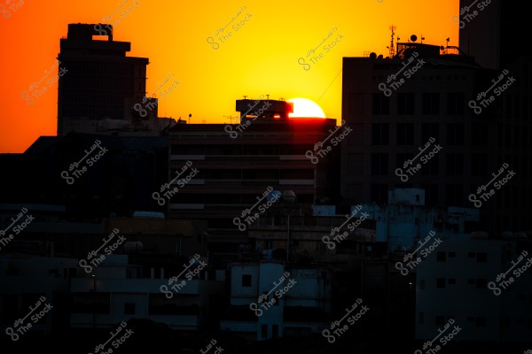 Sun setting behind city buildings with an orange gradient in the sky.