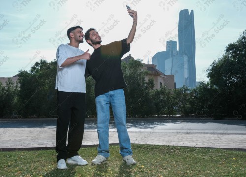 A snapshot of two young Saudis spending fun times in public parks with joy and enthusiasm, taking a selfie with a mobile phone