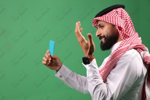 بورتريه رجل سعودي على خلفية خضراء متحمس يحمل بطاقة الصرافة مستعد للتسوق