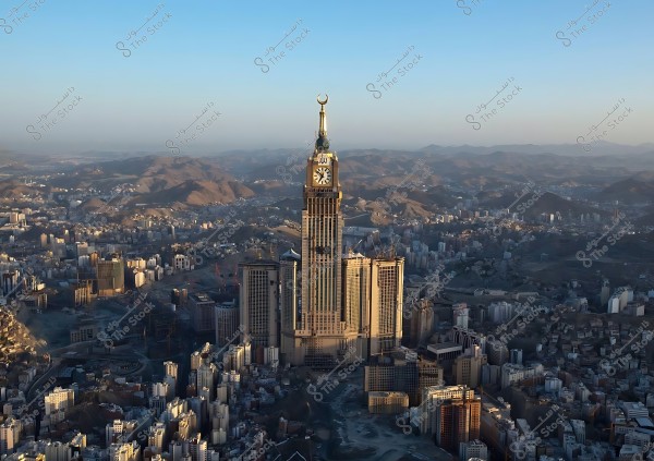 Aerial view of the Clock Tower in Mecca, centrally situated in the city with surrounding mountains in the background under a clear blue sky.