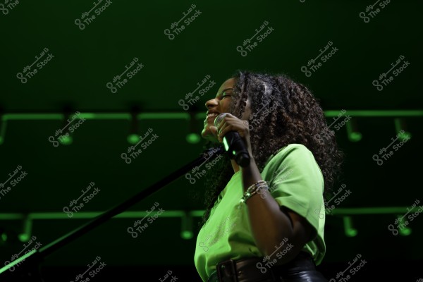 امرأة تحت الأضواء الخضراء تغني وتمسك ميكروفون.