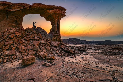 A shot of a group of rocky mountains and a man appears enjoying the sunset view.