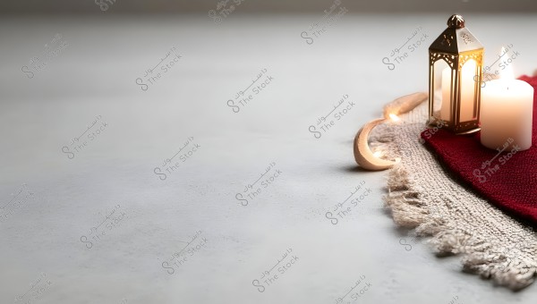 An image of a lit candle and a metal lantern placed on red and beige fabric. There is also a crescent-shaped decoration enhancing the scene. The setup gives a calm, spiritual, and traditional ambiance.