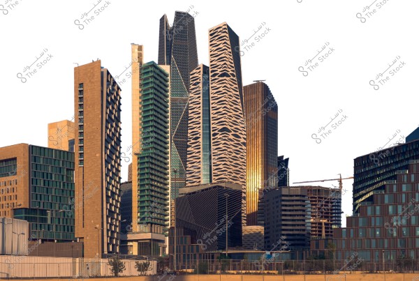 A view of a modern city skyline in Riyadh, Saudi Arabia. The image features a collection of skyscrapers with contemporary architectural designs, including glass buildings and structures with creative geometric patterns. The weather appears sunny and the sky is clear.