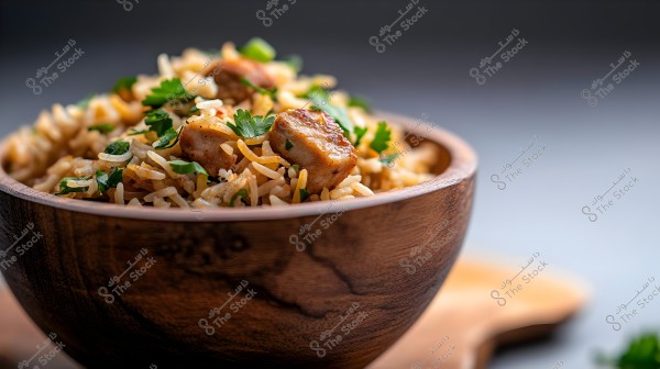 An image of a wooden bowl filled with cooked basmati rice, featuring chunks of browned meat and green cilantro leaves. The dish is presented attractively against a blurred background, highlighting the details of the rice and spices.