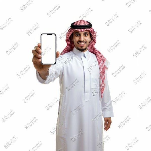 A portrait of a man wearing traditional Saudi attire, including a thobe and a shemagh, holding a smartphone with a blank white screen in his right hand against a white background. He appears to be presenting or displaying something on the phone with a friendly smile.