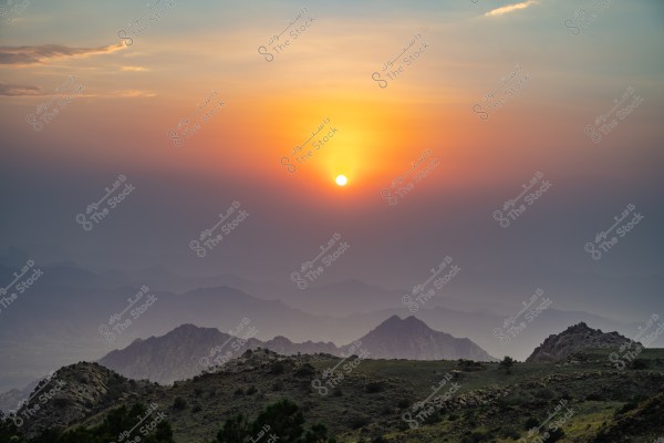 غروب الشمس خلف الجبال مع سماء ملونة بلون برتقالي وأزرق.