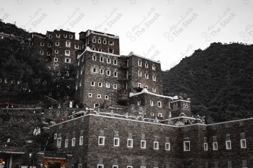 An ancient building built of stones in the middle of a group of windows surrounded by white paint while the sky looks cloudy during sunset, Rijal Almaa Heritage Village in the Asir region