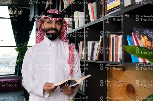 رجل سعودي يرتدي الزي السعودي التقليدي يتصفح أحد الكتب في المكتبة