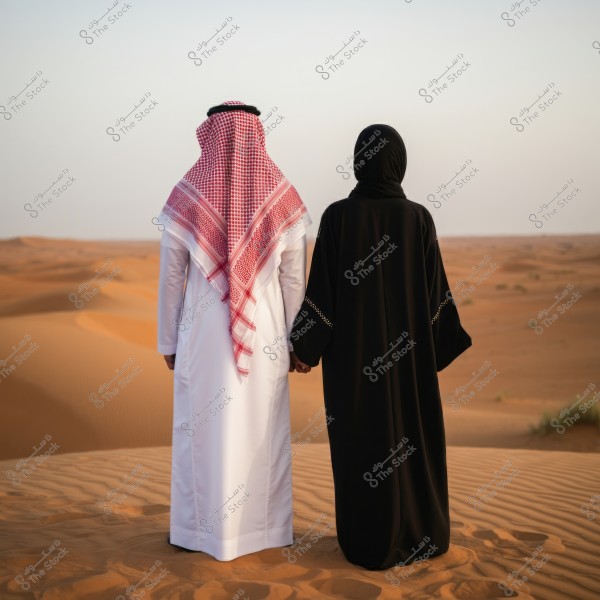 صورة لرجل وامرأة واقفين في صحراء. الرجل يرتدي ثوبًا أبيض وغترة حمراء, والسيدة ترتدي عباءة سوداء. يبدو الزوجان وكأنهما من منطقة الخليج العربي ويقفان على كثبان رملية شاسعة تحت سماء صافية.