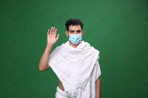 Portrait of a Saudi pilgrim on a green background wearing the Ihram to perform Hajj waving his hand in several directions