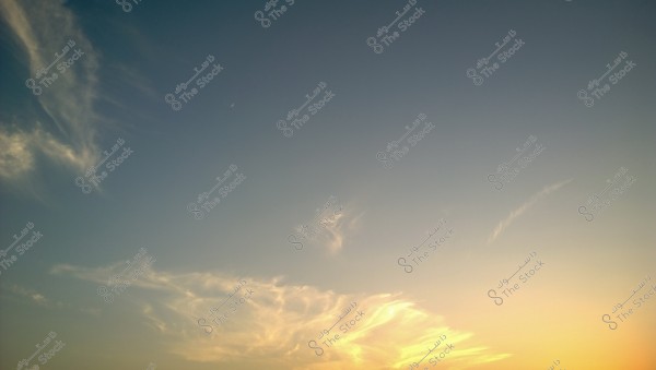 An image of the sky at sunset, displaying light clouds with colors ranging from light blue to yellow and orange. Some scattered clouds are visible on the horizon, with parts highlighted by the setting sun\'s light.