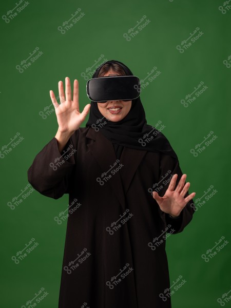 A woman wearing virtual reality goggles standing in front of a green background.