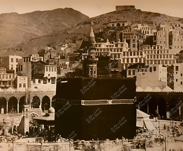 A vintage photo of the Kaaba in Mecca with surrounding buildings and mountains in the background.