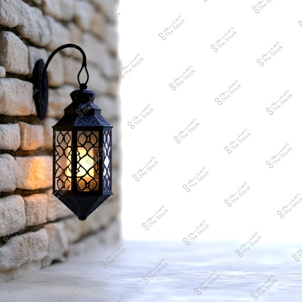 A metal lantern with Arabic design hanging on a stone wall, illuminated by warm yellow light. The wall is made of large white stones arranged neatly. The background is white, highlighting the intricate design of the lantern.