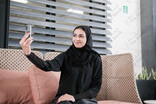 A Saudi woman wearing an abaya holds a mobile phone and displays its screen