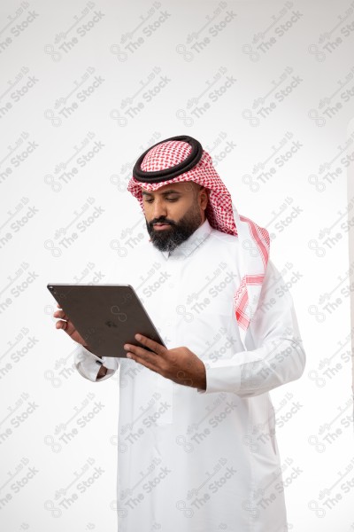 بورتريه رجل سعودي يحمل بيده الآيباد و ينظر لشاشته ويقوم بتعابير مختلفة، خلفية بيضاء