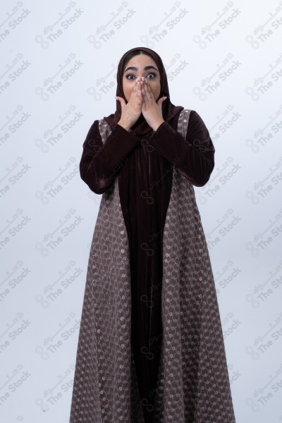 Portrait of a young Saudi woman wearing an abaya and hijab, with a smiling facial expression, standing against a white background